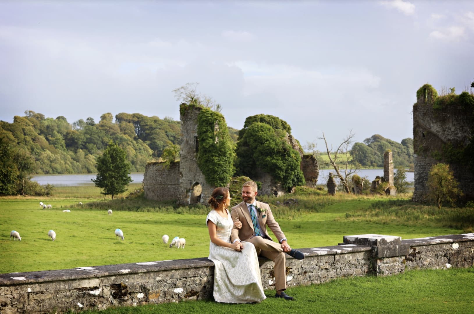 Wedding couple seated on the parkland wall at Temple House, the Templar castle and lake behind them
